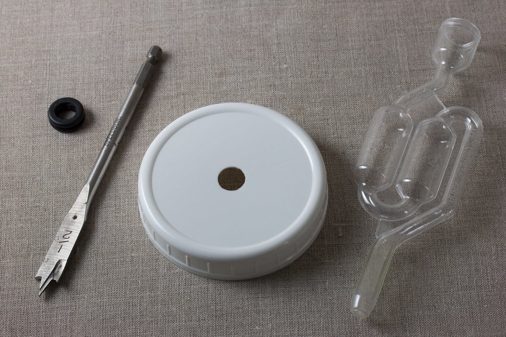 Photo of Star San foam in a fermentation vessel being swirled to coat all surfaces, airlock soaking in a jar of Star San solution